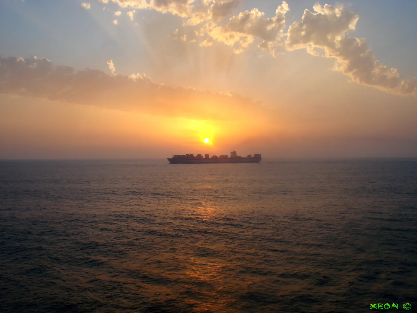 A container ship on the horizon at sea under an orange sunset
